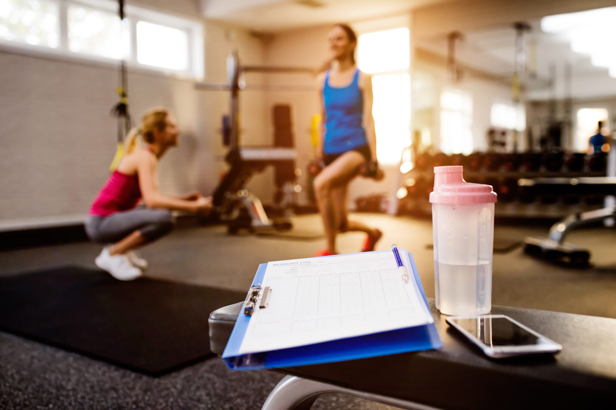 Gym close up, woman with personal trainer exercising squats, clipboard with work out plan, water bottle, smart phone